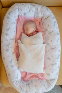 Ein Foto von einem Babyshooting. Zu sehen ist ein schlafendes Baby, das in seinem Nestchen liegt, aus der Vogelperspektive.