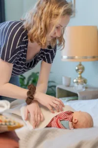 Ein Foto von einem Babyshooting. Zu sehen ist eine Mutter, die ihr schlafendes Neugeborenes gerade puckt.