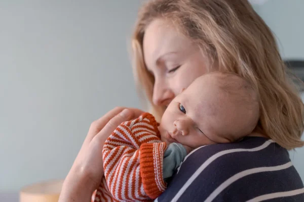 Eine Mutter trägt und kuschelt ihr Baby. Der Kopf des Babys liegt auf der Schulter der Mutter und die Mutter hat die Augen geschlossen.